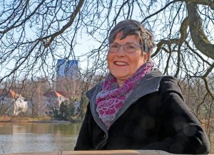 Frau mit grauen Haaren und Brille steht vor einem Teich